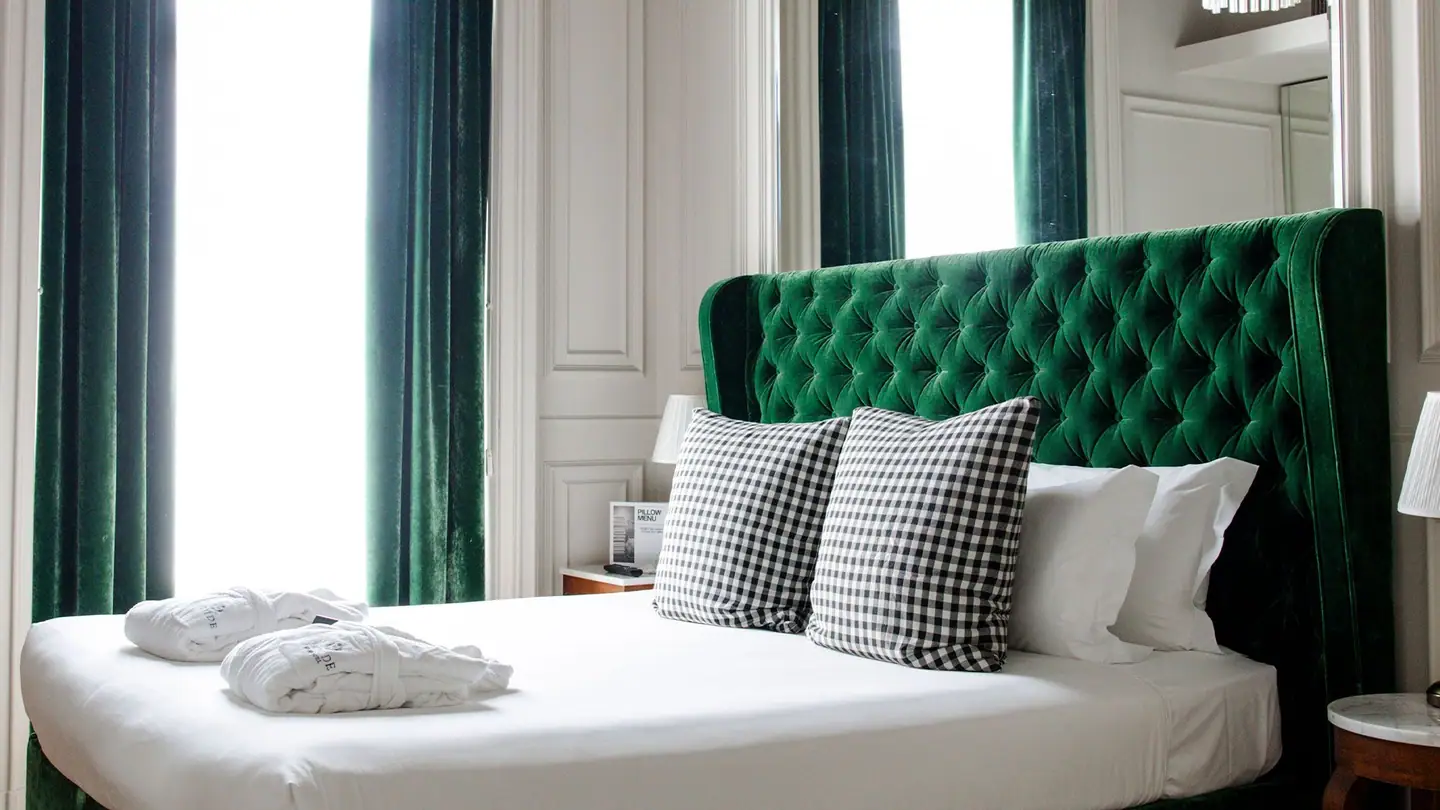 La Camera Deluxe: il letto con la testiera imbottita in velluto verde e i cuscini a quadri