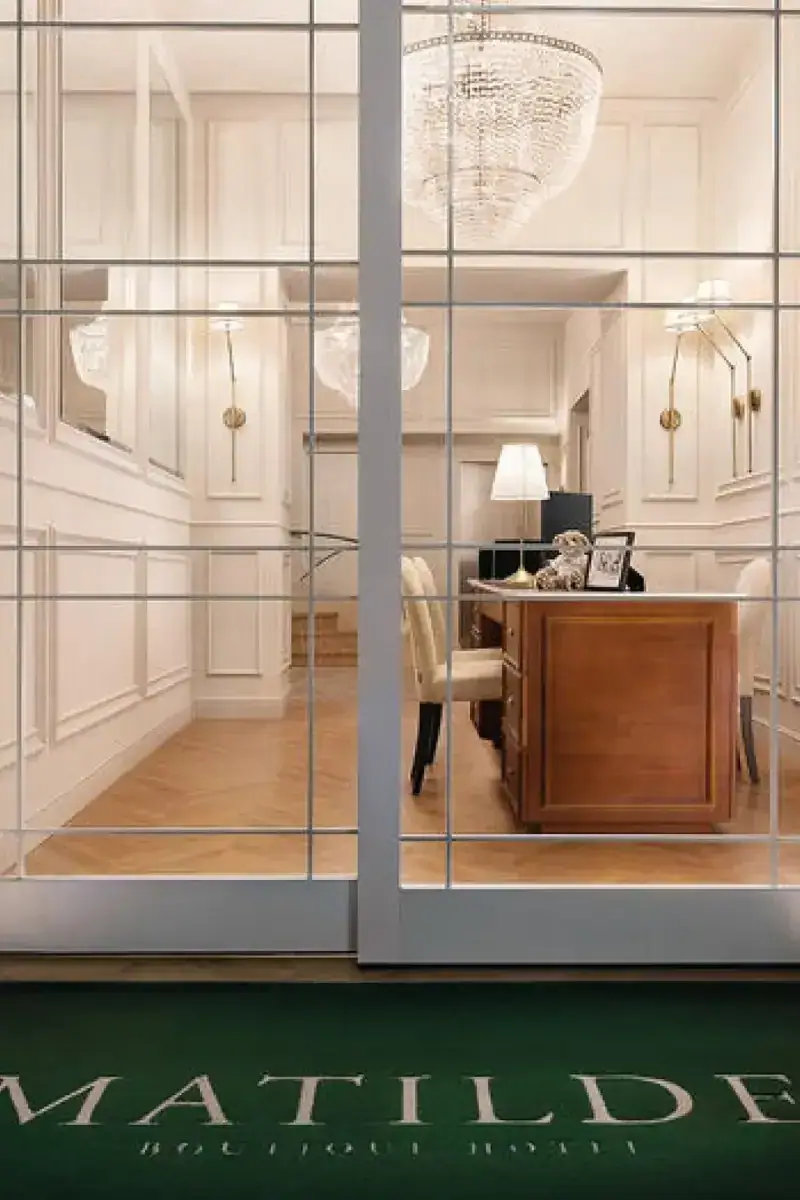 L'ingresso dell'hotel: le porte a vetri, i lampadari e il tappeto verde col nome Matilde